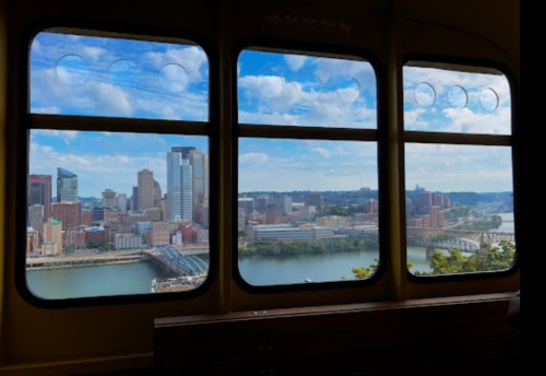 View of a city skyline with skyscrapers and a river, framed by three large windows under a blue sky.