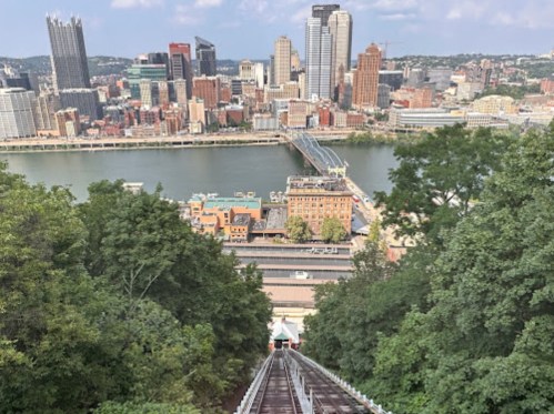 A view from a hilltop overlooking Pittsburgh, with a funicular railway and the city skyline in the background.
