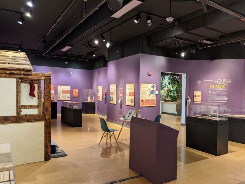 A museum exhibit featuring purple walls, display cases, and a wooden structure, showcasing various informational panels.