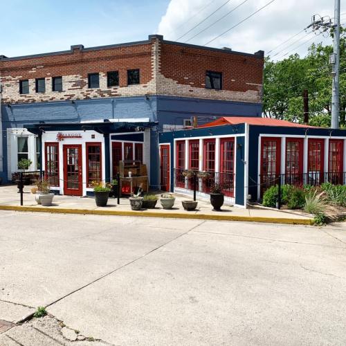 A colorful building with red and blue accents, featuring large windows and potted plants outside.