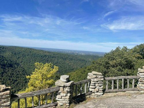 Scenic view from a stone overlook, showcasing lush green mountains and a clear blue sky.