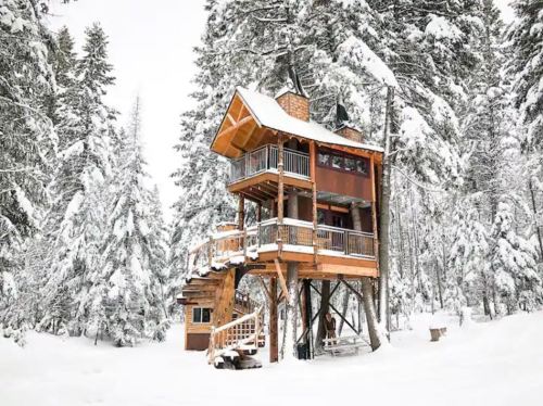 A wooden treehouse surrounded by snow-covered trees in a winter landscape.