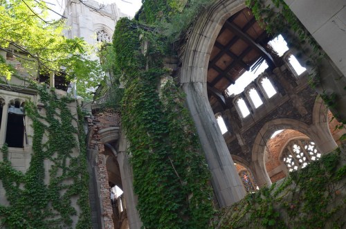 A view of a dilapidated building covered in ivy, showcasing crumbling walls and an open roof with sunlight filtering through.