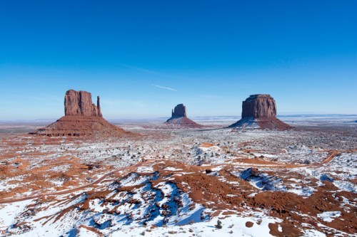 Snow-covered red rock formations under a clear blue sky in a desert landscape.