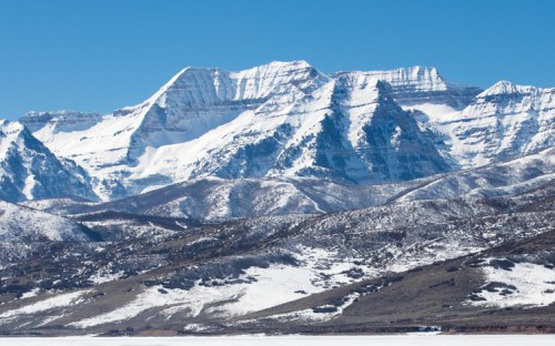Snow-capped mountains rise against a clear blue sky, with a snowy landscape in the foreground.
