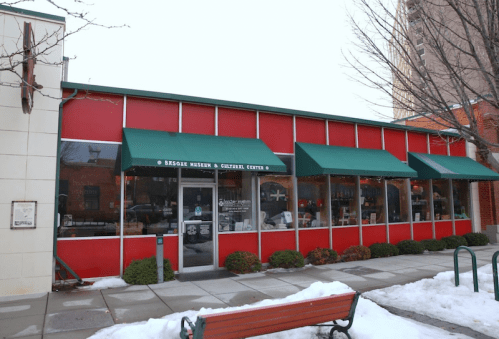 A red storefront with green awnings, featuring large windows and a snowy sidewalk in front.