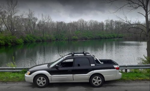 A black and white truck parked by a calm, green lake surrounded by trees under a cloudy sky.