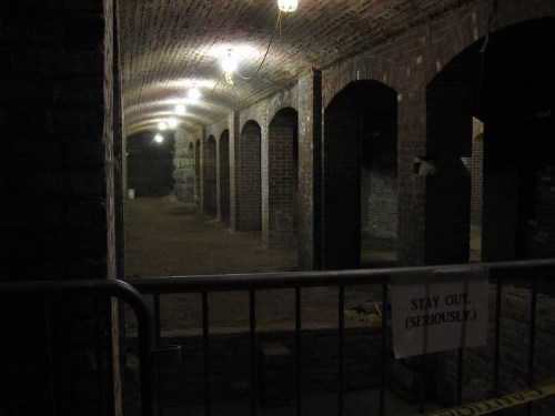Dimly lit underground space with brick arches and a "Stay Out (Seriously)" sign behind a barrier.