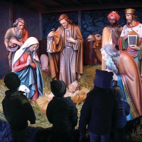 A nativity scene with Mary, Joseph, and baby Jesus, surrounded by onlookers and animals in a stable setting.