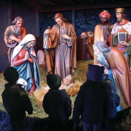 A nativity scene with Mary, Joseph, and baby Jesus, surrounded by onlookers and animals in a stable setting.