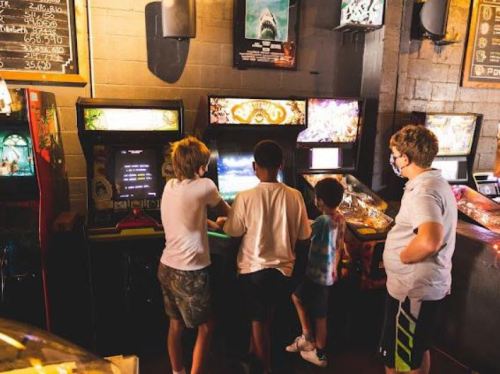 Four children are gathered around an arcade game, focused on the screen in a retro gaming environment.