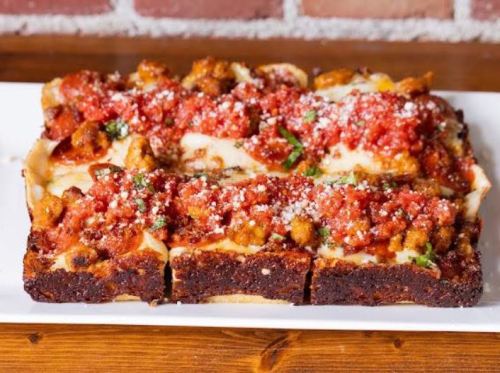 A rectangular pizza topped with marinara sauce, cheese, and herbs, served on a white plate against a brick background.