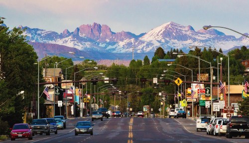 A scenic view of a small town street with mountains in the background, featuring shops and cars along the road.