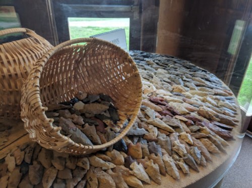 A woven basket spills various stone tools onto a circular display, showcasing a collection of artifacts.