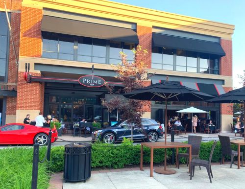 Exterior view of a restaurant named "Prime," featuring outdoor seating, umbrellas, and parked cars.