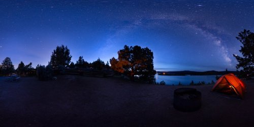 A serene campsite at night, featuring a glowing tent, a fire pit, and a stunning view of the starry sky and lake.