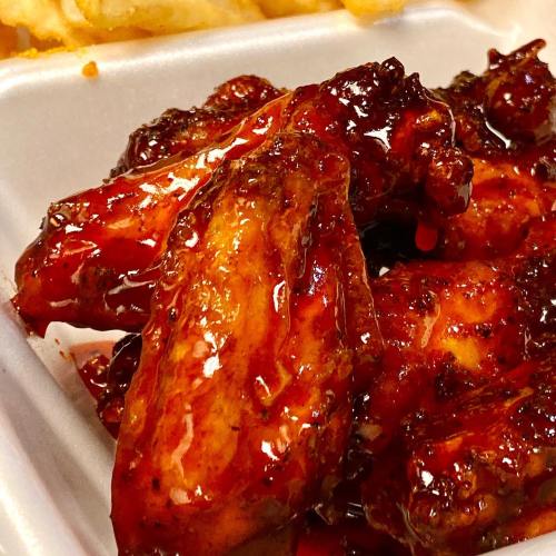 Close-up of glazed chicken wings, coated in a shiny, spicy sauce, served in a takeout container.