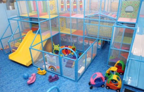 Colorful indoor play area with slides, soft play equipment, and toy cars scattered on the blue floor.
