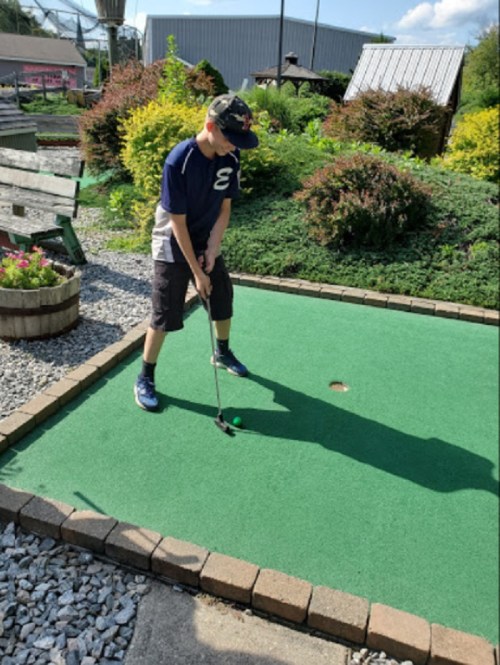 A child prepares to putt on a mini-golf course with green turf and landscaped surroundings.