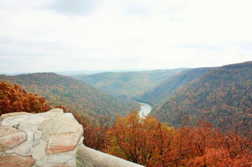 A scenic view of a valley with autumn foliage and a winding river, under a cloudy sky.
