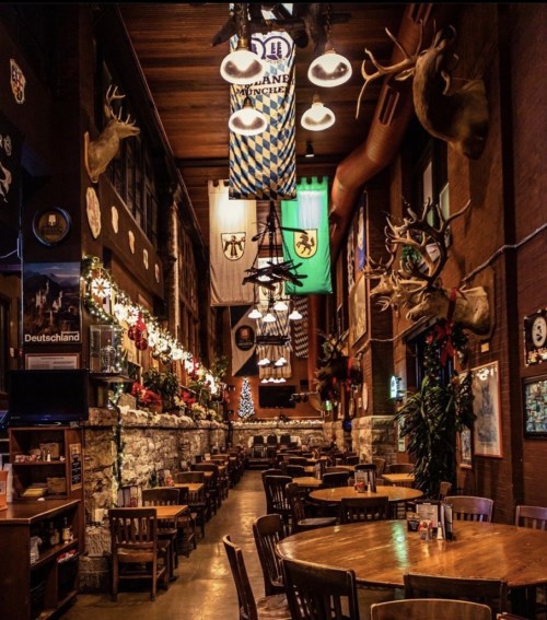A rustic restaurant interior with wooden tables, antler decor, and festive decorations, featuring banners and stone walls.