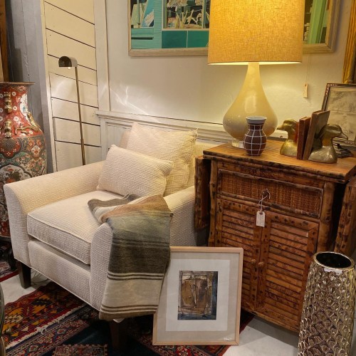 Cozy living space featuring a beige armchair, decorative lamp, and artwork against a backdrop of stylish decor.