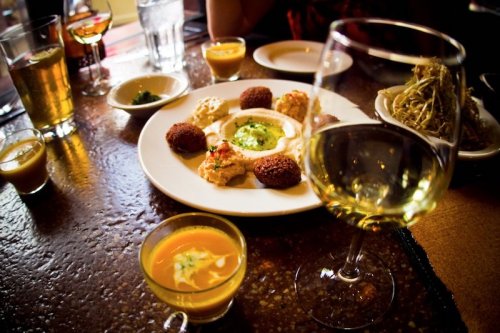 A table set with various dishes, including dips and falafel, alongside drinks in glasses.