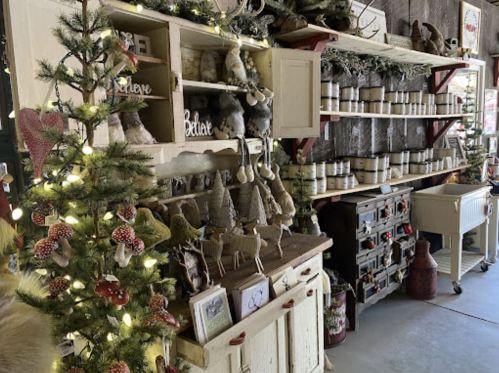 A cozy shop display featuring holiday decorations, candles, and rustic decor, with a small tree adorned with lights.