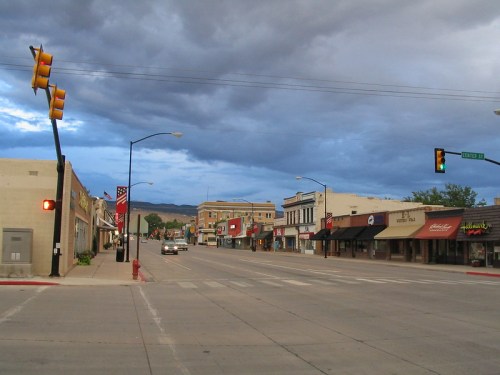 A quiet downtown street with shops and traffic lights under a cloudy sky.