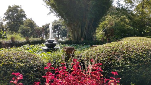 A serene garden scene featuring a fountain surrounded by lush greenery and vibrant red flowers.