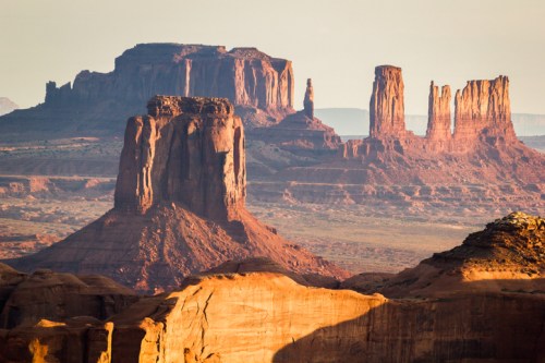 A scenic view of red rock formations and mesas under a soft golden light in a desert landscape.