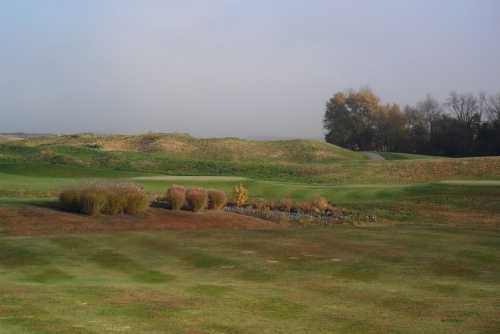 A serene golf course landscape with rolling hills, patches of grass, and a small stream surrounded by shrubs.