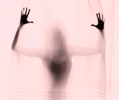 A silhouette of a person with hands pressed against a sheer curtain, creating a ghostly effect.