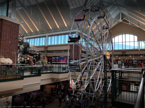 A colorful indoor Ferris wheel in a shopping mall, surrounded by festive decorations and shops.