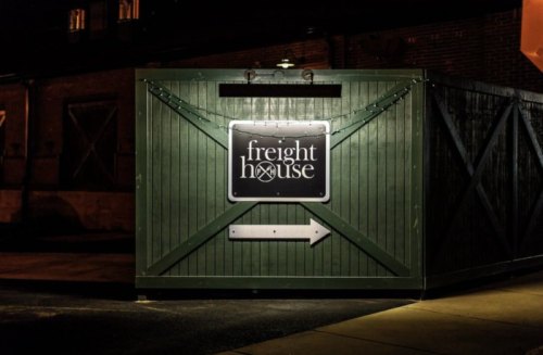 A green wooden structure at night with a sign reading "freight house" and an arrow pointing to the right.