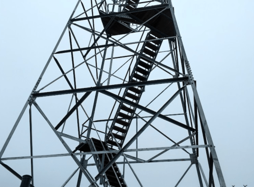 A tall metal tower with a staircase winding up, set against a foggy sky.
