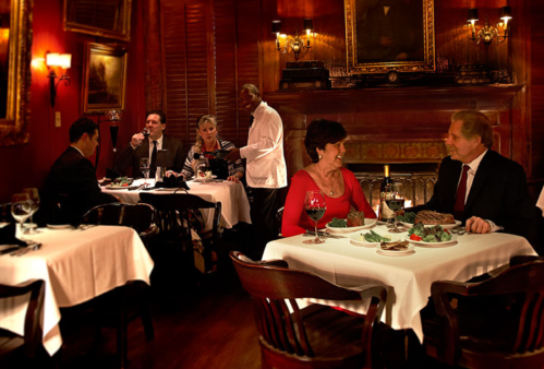 A cozy restaurant scene with diners at tables, a waiter serving, and elegant decor featuring red walls and soft lighting.