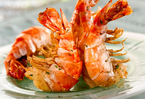 Close-up of cooked shrimp on a plate, garnished with herbs, showcasing their vibrant orange color and texture.