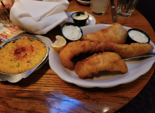 A plate of golden fried fish fillets with tartar sauce and a side of creamy corn casserole.