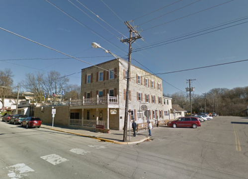 A historic building at a street corner with parked cars and people walking nearby on a clear day.