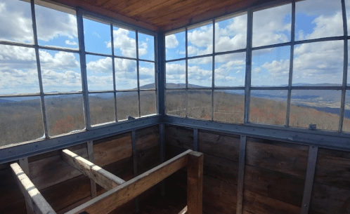 View from inside a lookout tower, featuring large windows and a scenic landscape of mountains and blue skies.