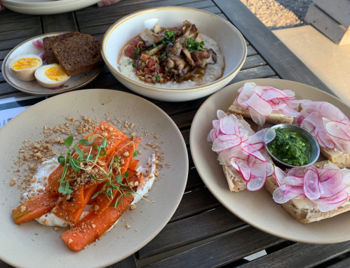 A table with three dishes: roasted carrots with nuts, a savory bowl, and bread topped with radishes and pesto.