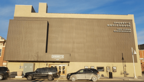 Exterior of Sperry's Moviehouse, a two-story building with a sign, parked cars in front, and a clear blue sky.
