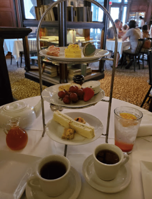 A tiered dessert stand with various pastries, fruits, and drinks, accompanied by two cups of coffee on a table.