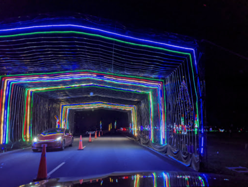 A colorful light tunnel with vibrant blue, green, and red lights, viewed from a car on a dark road.