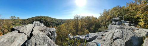 Panoramic view of rocky outcrop overlooking a forested valley under a clear blue sky. Sun shining brightly.