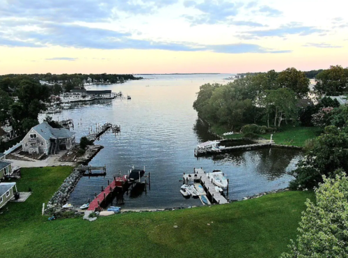 A serene waterfront view at sunset, featuring boats, docks, and lush greenery along the shore.