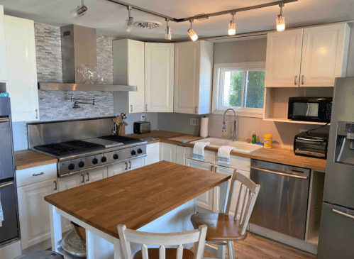 Modern kitchen with white cabinets, stainless steel appliances, a wooden table, and a large gas stove. Bright and spacious.