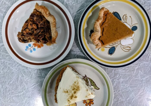 Three slices of pie on decorative plates: pecan, pumpkin, and cream pie, arranged on a textured surface.