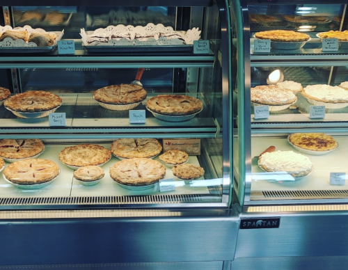 A display case filled with various pies, including fruit and cream varieties, all labeled with names.